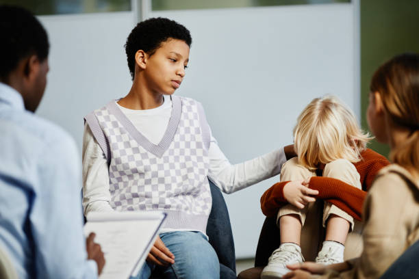 Portrait of teenage girl comforting little boy crying in group therapy session with diverse children