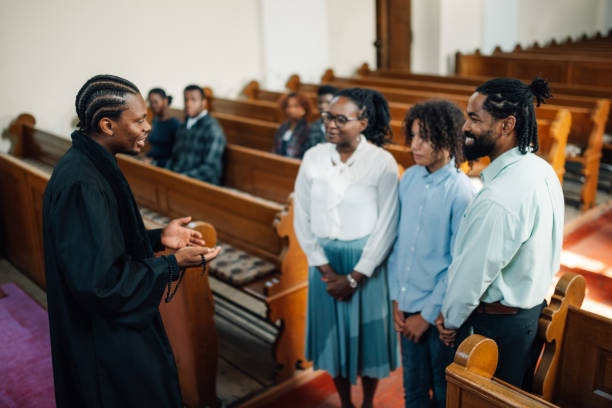 Priest is standing in a church, talking to a family after a service. The family is listening attentively to the priest