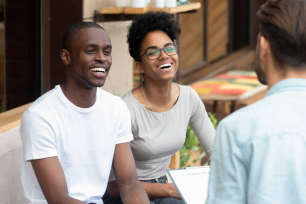 Happy african american young family couple listen to counselor psychologist salesman Real Estate Agent consult black clients talk to patients customers holding clipboard at meeting, marriage therapy counseling