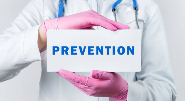 Cropped view of young female doctor in a white coat and pink sterile gloves holding a card with text PREVENTION. Medical concept.